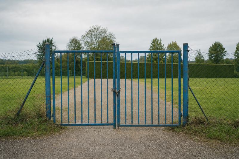 Geschlossenes Tor zu einem Dorfsportplatz, Kette und Maschendrahtzaun, Kiesweg dahinter