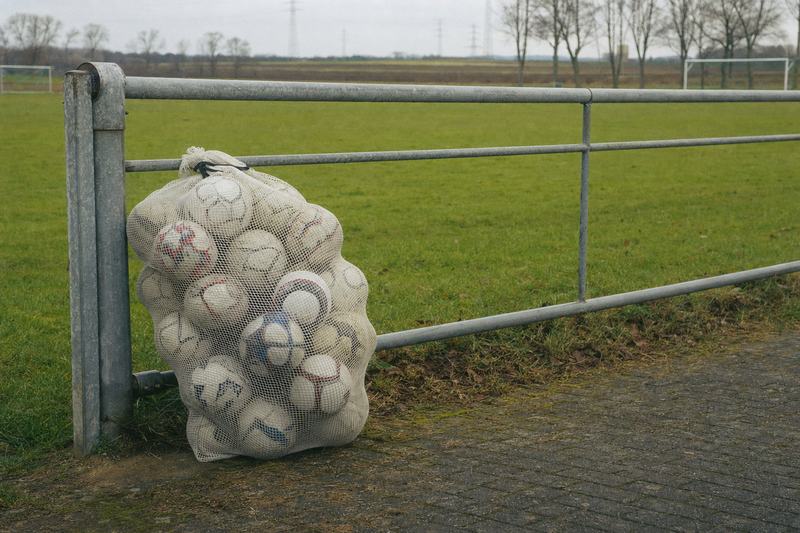 Netzsack mit Bällen, an ein niedriges Metalltor am Rand eines Trainingsplatzes gelehnt