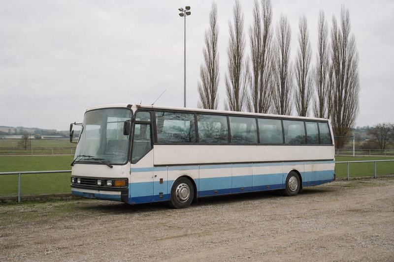 Älterer Reisebus, geparkt auf Kies neben einem Sportplatzzaun