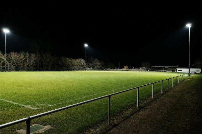 Leerer Sportplatz bei Nacht unter Flutlicht, Absperrgitter an der Seitenlinie