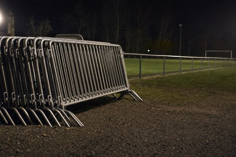 Aufgereihte mobile Absperrgitter am Rand eines Sportplatzes bei Nacht