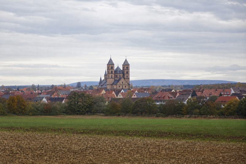Türme eines romanischen Doms über den Dächern einer Kleinstadt, von den Feldern gesehen